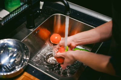 Cropped hands of woman washing tomatoes at kitchen