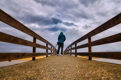 Rear view of man walking on bridge against sky