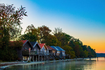 House and trees by lake against clear blue sky