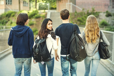 Rear view portrait of smiling teenager walking with friends on bridge