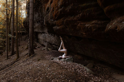 Woman in acrobatic pose in front of a high rock wall in a forest