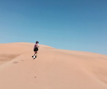 Woman walking on sand dune against clear sky at desert