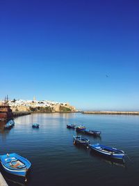 Boats moored in sea against clear blue sky