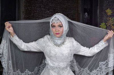 Portrait of bride wearing traditional clothing sitting against wall