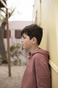 Portrait of a teenage boy leaning against wall looking away