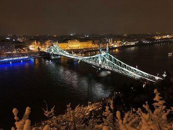 Illuminated bridge over river in city against sky at night