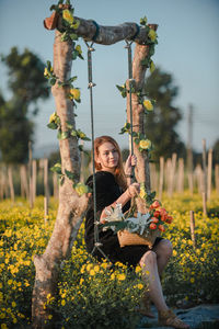 Happy woman holding flowers sitting on rope swing