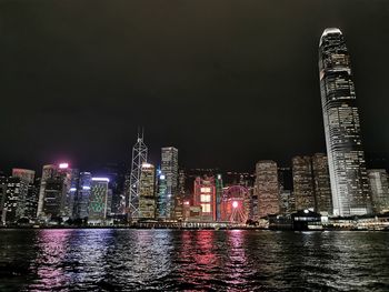 Illuminated buildings by river against sky at night