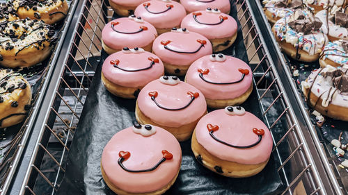 Pink donuts with a smile in a metal tray on a store shelf, side view close-up.