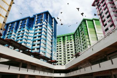 Low angle view of pigeons flying amidst buildings at rochor centre