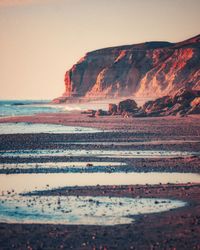 Scenic view of sea against clear sky and a beautiful cliff shot at sunset