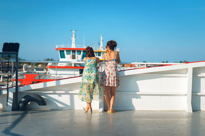 Rear view of women standing against blue sky