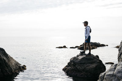 Man standing on rock by sea against sky