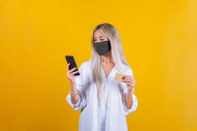 Young woman using mobile phone against yellow wall