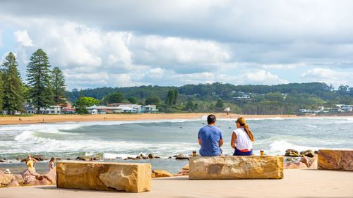 Rear view of men sitting on shore against sky