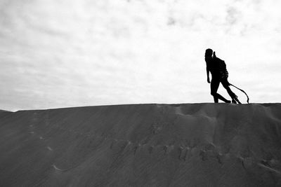 Model with costume wing walking at desert against cloudy sky