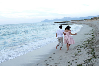 Rear view of women standing on beach against sky