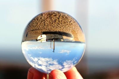 Cropped image of person holding glass ball with upside down reflection