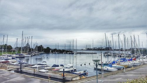 Boats moored at harbor against cloudy sky