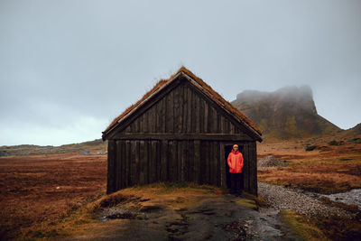 Young tourist standing near hut between wild lands near high stone hills and cloudy sky