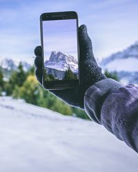 Close-up of hand photographing on snow covered mountain