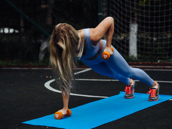Young beautiful blond woman with long hair in light blue activewear do exercises with bar bells 