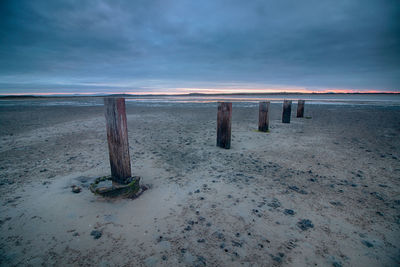 Wooden posts on beach against sky during sunset