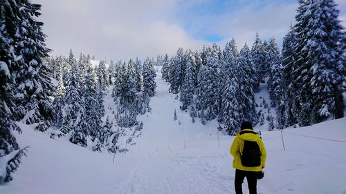 Rear view of man walking on snow covered mountain against sky