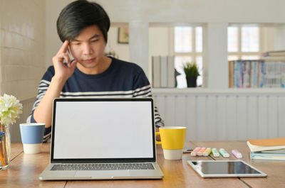 Mid adult man using mobile phone while sitting on table