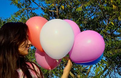 Rear view of girl holding balloons against tree