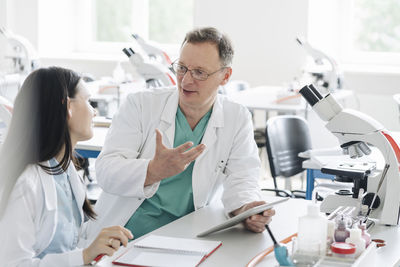 Teacher and student in white coats talking and using tablet in lab