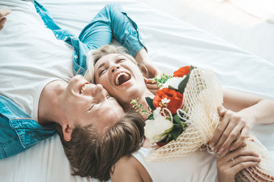 Happy couple with bouquet lying on bed in home