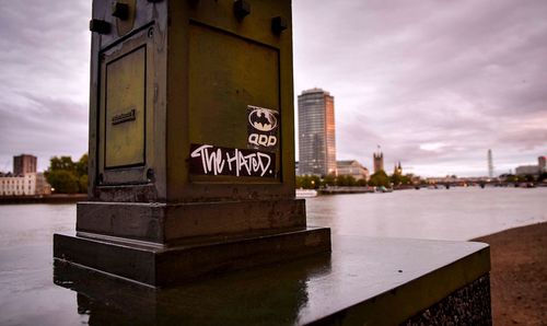 Information sign by river against cloudy sky