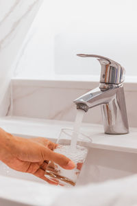 Man filling glass of water at sink in bathroom