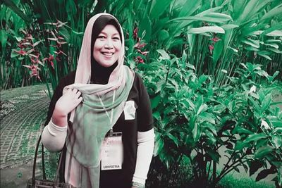 Portrait of smiling young woman standing against plants
