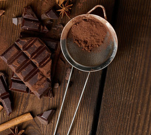 Broken pieces of dark chocolate, cinnamon sticks and star anise on a brown wooden table, top view