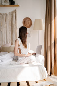 Woman using laptop while sitting on bed at home