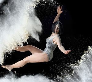 Full length of woman dancing with splashing powder against black background