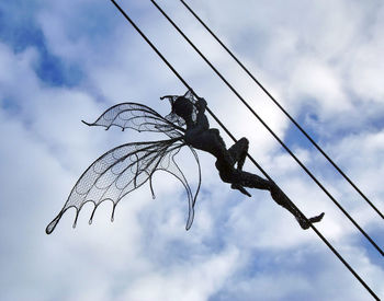 Low angle view of bird perching on power line against cloudy sky