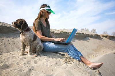 Young woman working on laptop outdoors in company of her dog