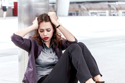 Tensed young businesswoman sitting on walkway 