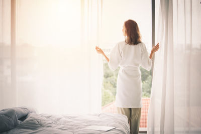 Rear view of woman standing on bed