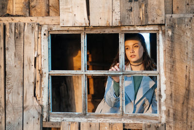 Girl looks out the window from an old wooden house, sunlight