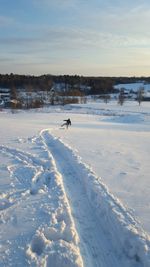 Distant view of person on snow covered field against sky