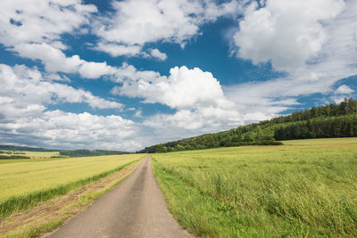 Street amidst grassy field against cloudy sky