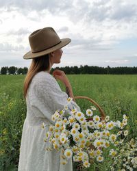 Woman standing by flowers on field against sky