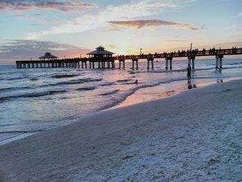 Pier on beach against sky during sunset