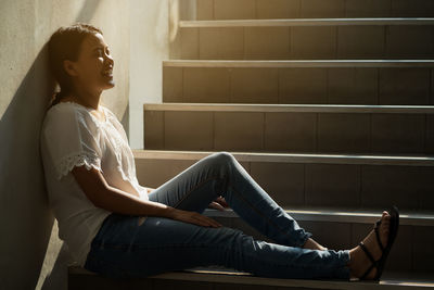 Side view of young woman sitting on staircase against wall