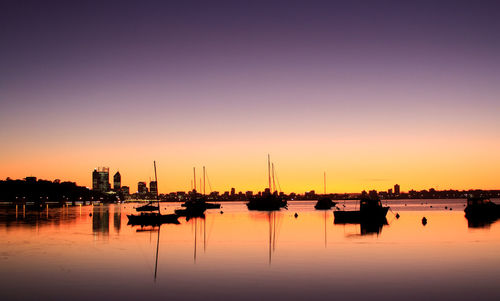 Silhouette boats moored in sea with reflection against clear purple sky