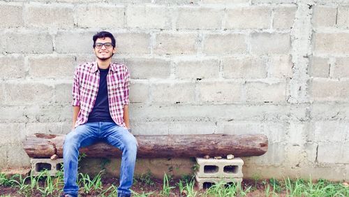 Portrait of smiling young man sitting on brick wall